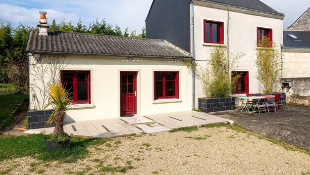A two-story house with a tiled roof, red-framed windows, and a small patio area with outdoor furniture.