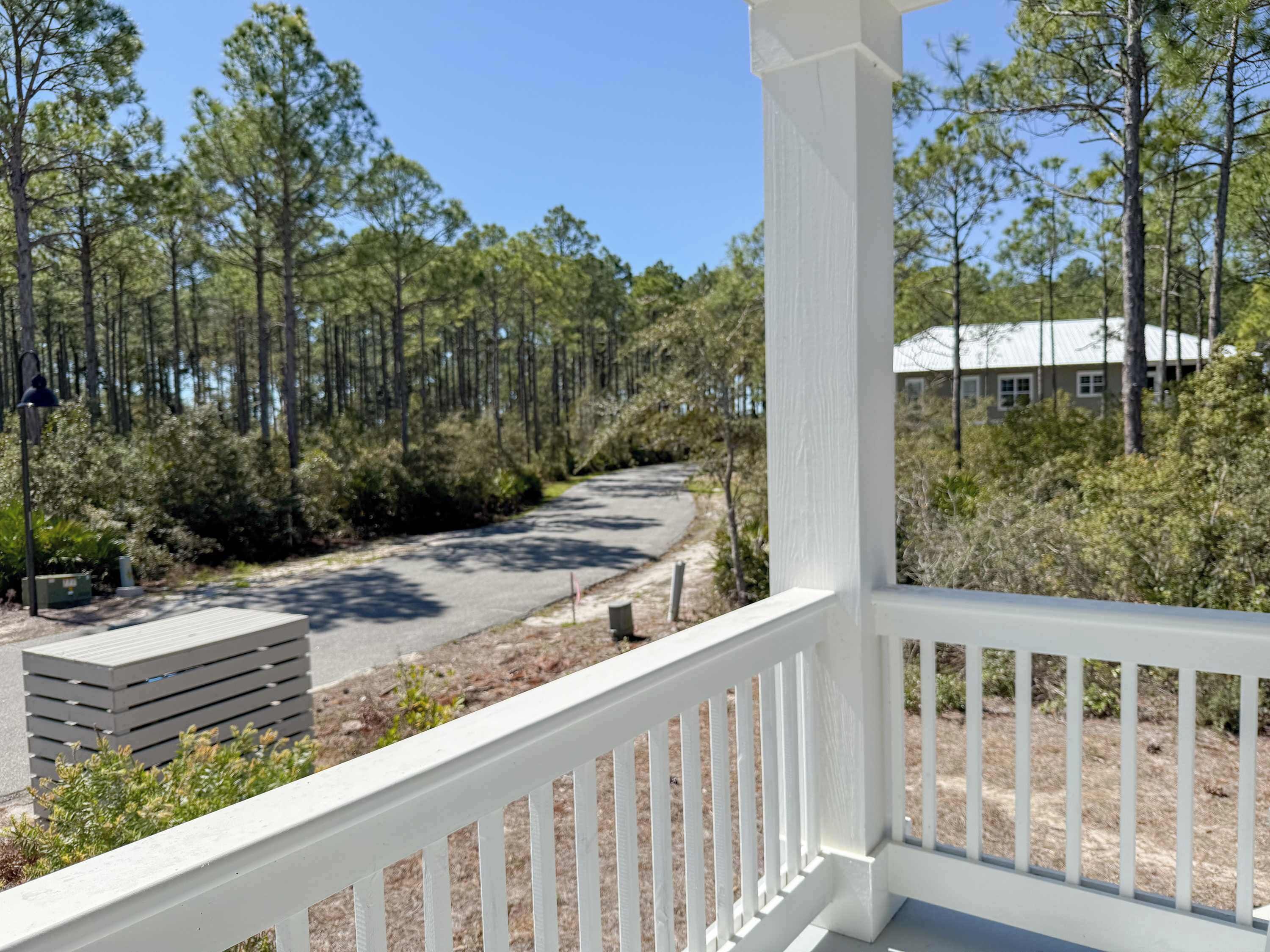 A white wooden deck with a view of a forested area and a building in the background.