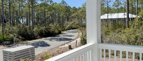 A white wooden deck with a view of a forested area and a building in the background.