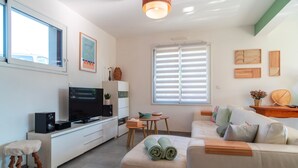 A modern living room with a sofa, a TV, a small table, and a window with blinds.