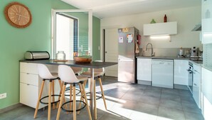 A modern kitchen with a dining area, featuring a refrigerator, dishwasher, and a small island with stools.