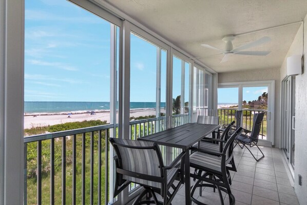 Een balkon met uitzicht op het strand, een tafel met stoelen en een plafondventilator.