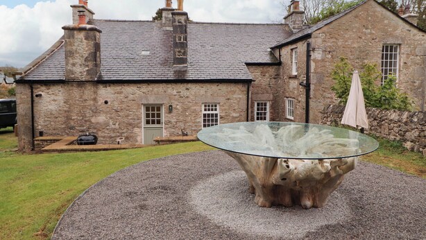 Un edificio de piedra con diseño tradicional, que presenta una gran mesa de cristal en primer plano.