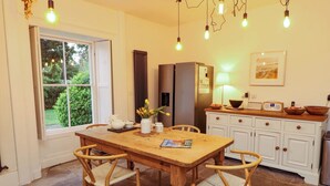 Un comedor con mesa y sillas de madera, un refrigerador, una encimera de cocina con electrodomésticos y una ventana con vistas al verdor.