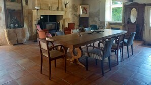 A rustic dining area with a large wooden table, multiple chairs, a fireplace, and a stone wall.