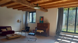 A room with a wooden ceiling, a red sofa, a black chair, a wooden cabinet, and a window with curtains.