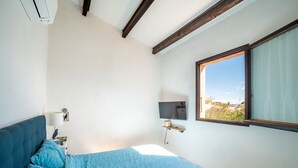 A bedroom with a bed, a nightstand, a lamp, a TV, and a window with a view. - L’Échappée Méditerranéenne - Proche Plage (Leucate)