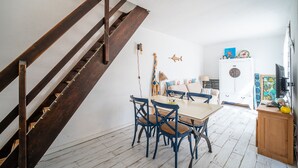 A dining area with a wooden staircase, a white refrigerator, and a TV on a wooden cabinet. - L’Échappée Méditerranéenne - Proche Plage (Leucate)