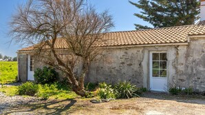 A rustic stone building with a tiled roof, a single door, and a small garden area with plants and a tree. - L’Échappée du Port - Grand Jardin (Bouin)