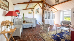 A rustic interior with exposed wooden beams, a dining area with wicker furniture, and a view through a glass door. - L’Échappée du Port - Grand Jardin (Bouin)