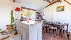A rustic kitchen with wooden beams, a dining area with a table and chairs, and a cactus plant. - L’Échappée du Port - Grand Jardin (Bouin)