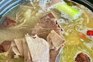 Een pan met heldere bouillon, vlees en groenten.