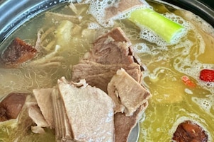 Una olla con caldo claro que contiene carne y verduras.