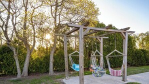 A wooden swing set with two swings and a hanging hammock in a backyard.