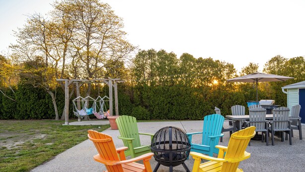 An outdoor patio with Adirondack chairs, a fire pit, and a swing set.