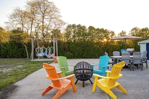 An outdoor patio with Adirondack chairs, a fire pit, and a swing set. - Cozy Cottage Mins 2 Beach - Outdoor Dining & Firepit (Berlin)