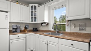 A kitchen with white cabinets, a granite countertop, a stainless steel sink, and a window with a view of trees.