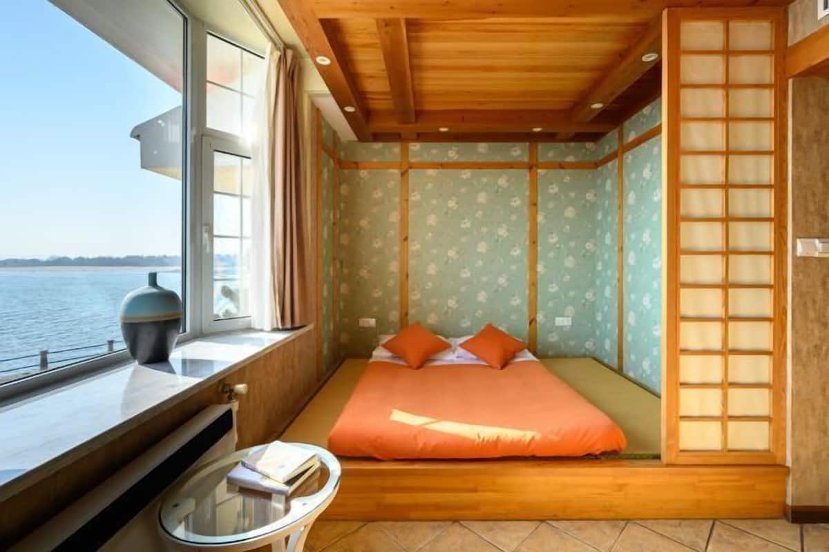 Ein Zimmer mit einem Bett, einem kleinen Tisch und Blick auf das Wasser.