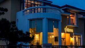 Ένα σύγχρονο ξενοδοχείο με καμπυλόγραμμη πρόσοψη, μεγάλα παράθυρα και μια επιβλητική επιγραφή με την ονομασία «Villatan».