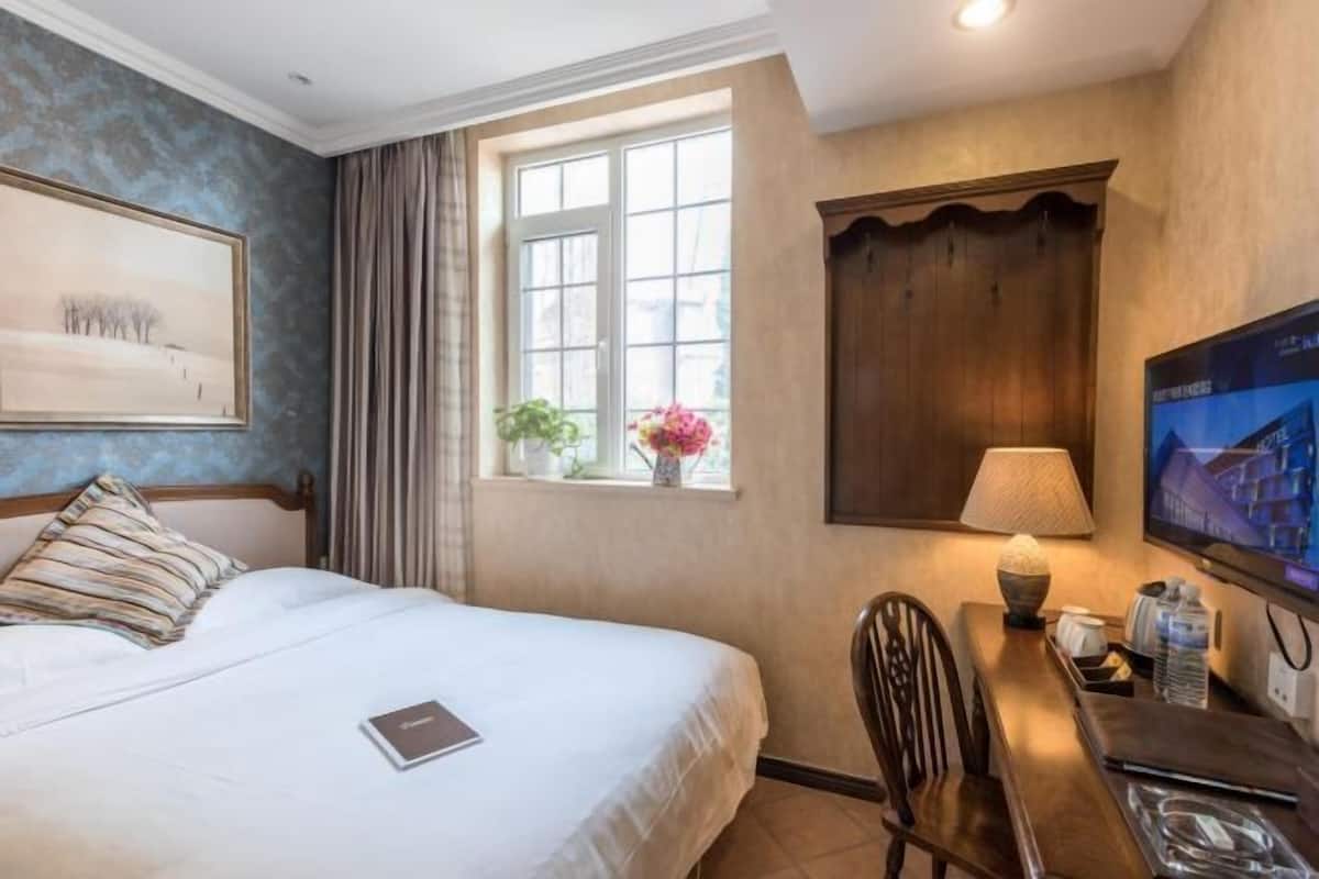 Ein Hotelzimmer mit Bett, Schreibtisch mit Lampe, Fernseher und einem Fenster mit Vorhängen.