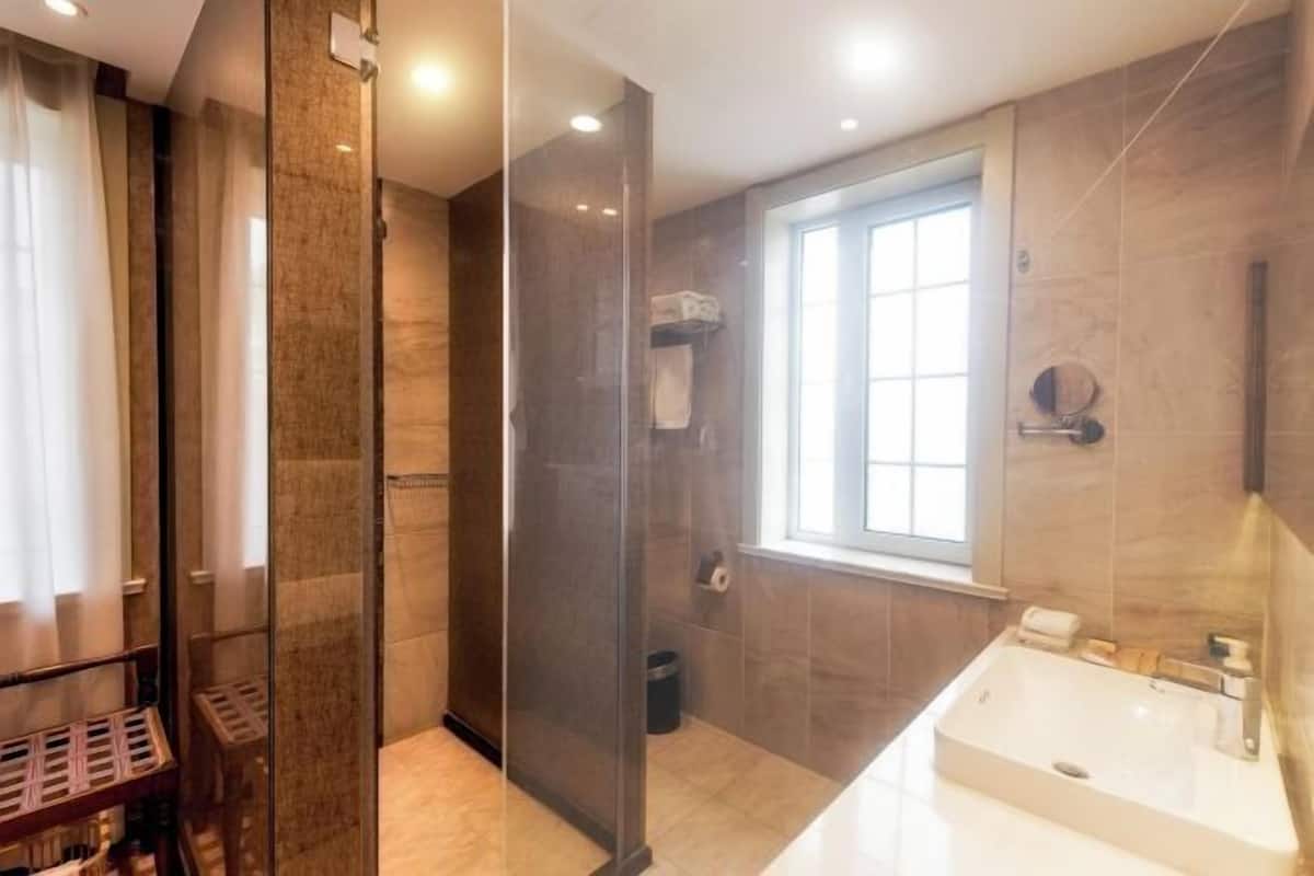 Ein modernes Badezimmer mit einer gläsernen Duschkabine, einem großen Fenster und einem weißen Waschbecken.