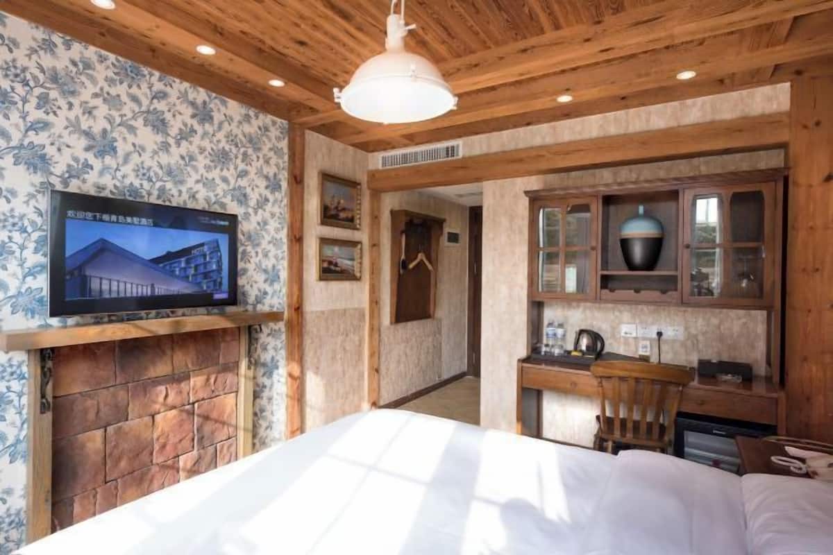 Ein Schlafzimmer mit Bett, Wand-Fernseher, Kamin, Schreibtisch mit Stuhl und einer Schrank mit Glastüren.