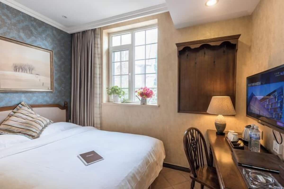 Ein Hotelzimmer mit einem großen Bett, einem Schreibtisch mit Stuhl, einem Fernseher und einem Fenster mit Vorhängen.