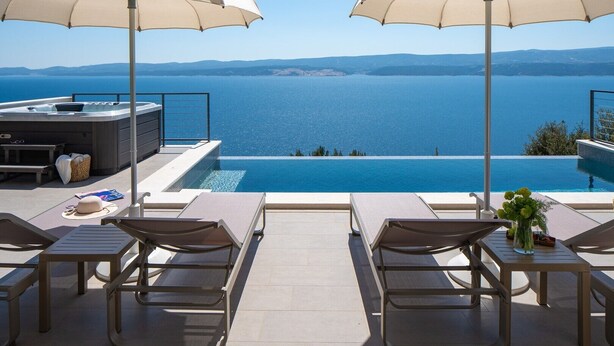 Zona junto a la piscina con dos sombrillas, sillas de descanso, un jacuzzi y vistas al mar.
