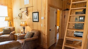 A wooden interior with a sofa, two lamps, a ladder, and a door leading to another room.