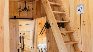 A wooden cabin interior with a spiral staircase, a chandelier, and a sign indicating the presence of a ladder.