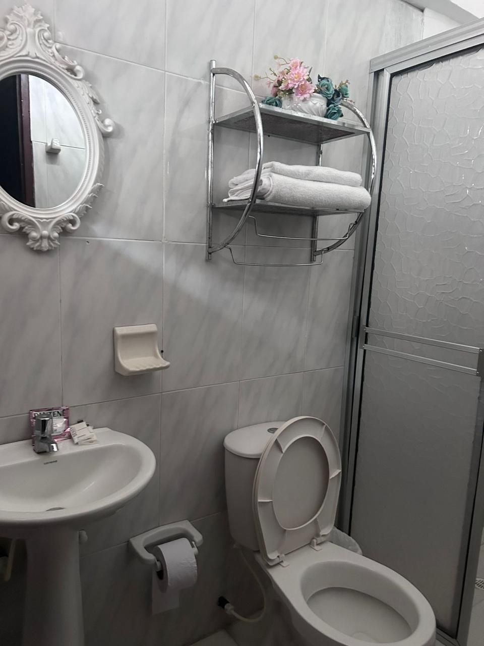 Ein Badezimmer mit Waschbecken, Toilette, Spiegel mit aufwendigem Rahmen, Ablagefläche mit Handtüchern und Duschbereich.