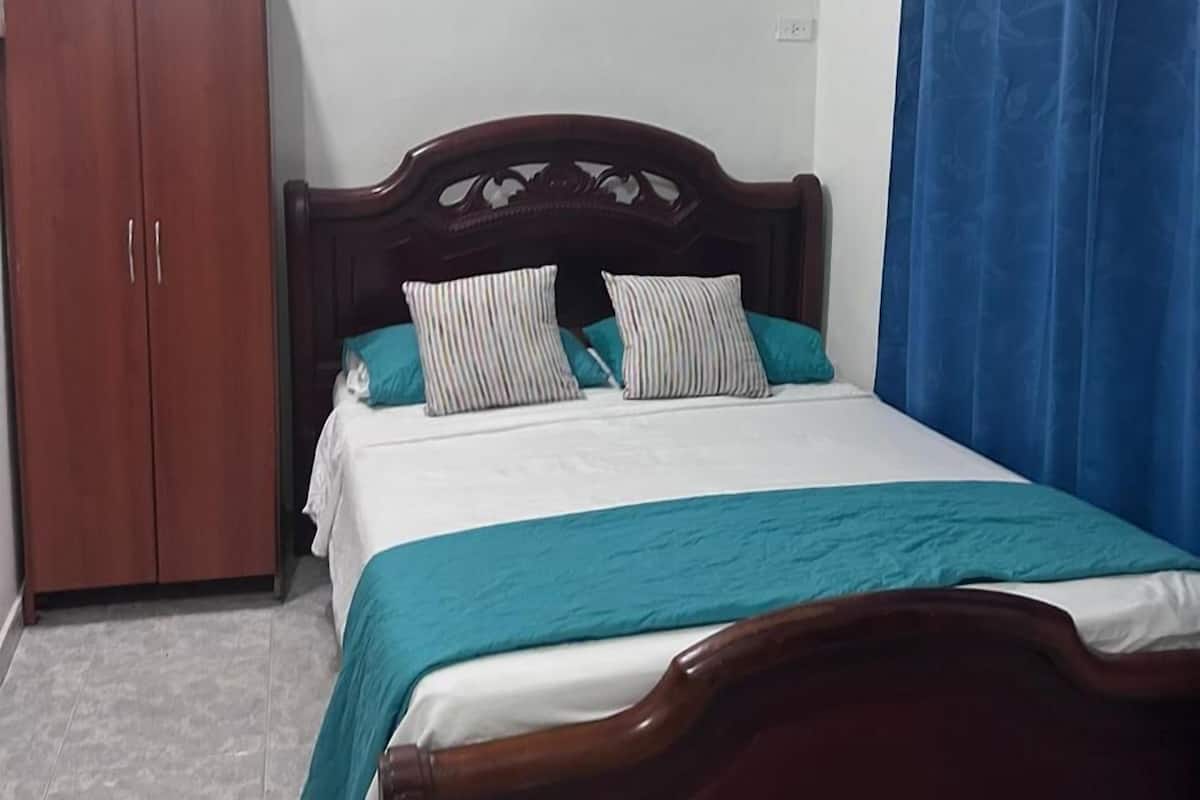 Un dormitorio con cama de madera, ropa de cama color verde azulado, ventilador de techo, aire acondicionado y armario.