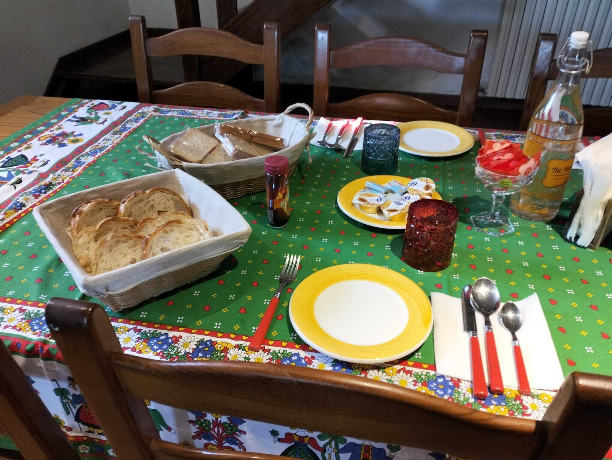 Une table à manger dressée avec du pain, des assiettes, des couverts et des condiments.