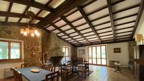 A spacious dining area with a stone wall, wooden ceiling beams, and a fireplace.