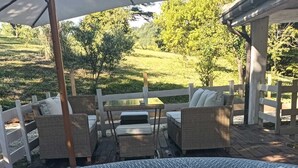 A hot tub with a wicker surround, wooden deck chairs, and a covered seating area with a view of a landscaped garden.