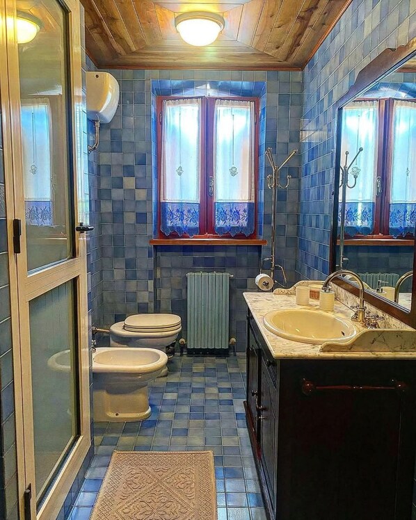 A bathroom with two toilets, a sink, a mirror, and a window with curtains.