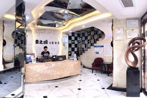Zona de recepció d'hotel amb un taulell de marbre, una recepcionista, una escala amb dibuix de quadradets i una gran escultura abstracta.