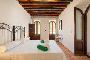 A bedroom with a bed, wooden ceiling, two arched windows, and a door.