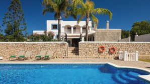 Una piscina con sillas de descanso, un muro de piedra y un edificio con balcón al fondo.