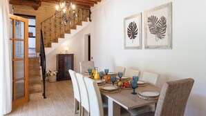 Un comedor con una mesa de madera dispuesta para el desayuno, una escalera con barandilla de hierro forjado y dos obras de arte con hojas enmarcadas en la pared.