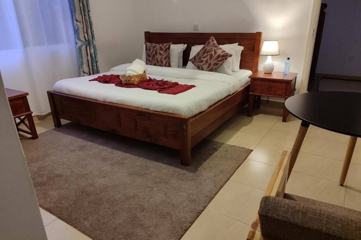 Ein ordentlich eingerichtetes Schlafzimmer mit einem hölzernen Bett, einem Nachttisch mit Lampe, einem kleinen Tisch mit einer Flasche und einem Stuhl.