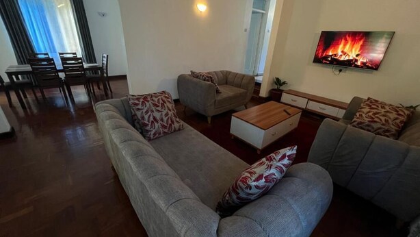 Ein Wohnzimmer mit einer Sofagarnitur, einem Couchtisch und einem an der Wand befestigten Fernseher.