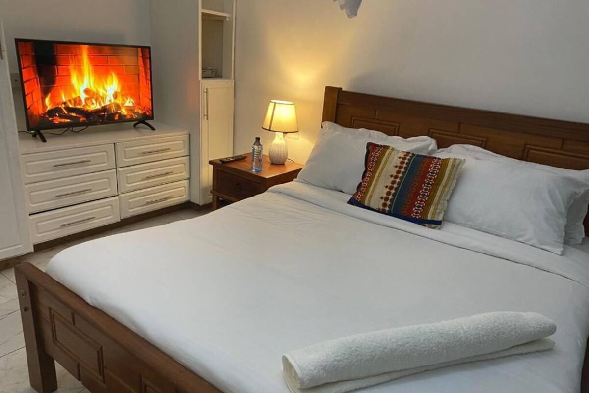 Ein ordentlich bezogenes Bett mit weißen Leinentüchern, einem Holz-Kopfteil und einem farbenfrohen Kissen.