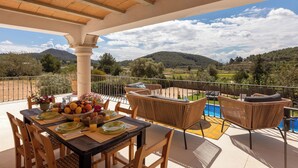 Ein überdachter Außenbereich zum Essen mit Korbmöbeln, einem Pool und Bergblick.