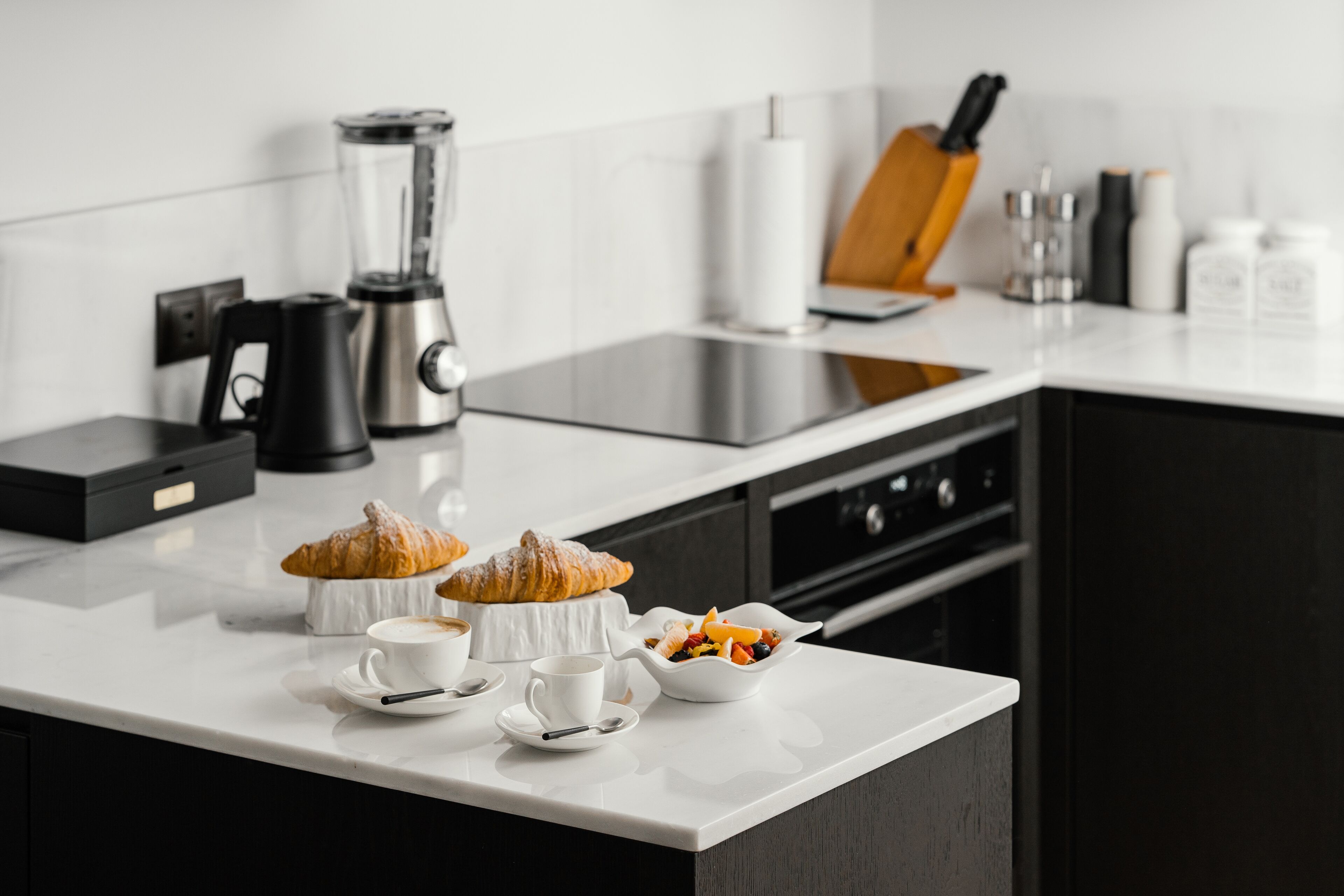 Une cuisine moderne dotée d’un plan de travail blanc, d’une machine à café, d’un mixeur et d’un bloc à couteaux.