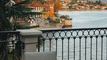 Un balcone con un tavolo apparecchiato per il tè, affacciato su un fiume con edifici e montagne sullo sfondo.