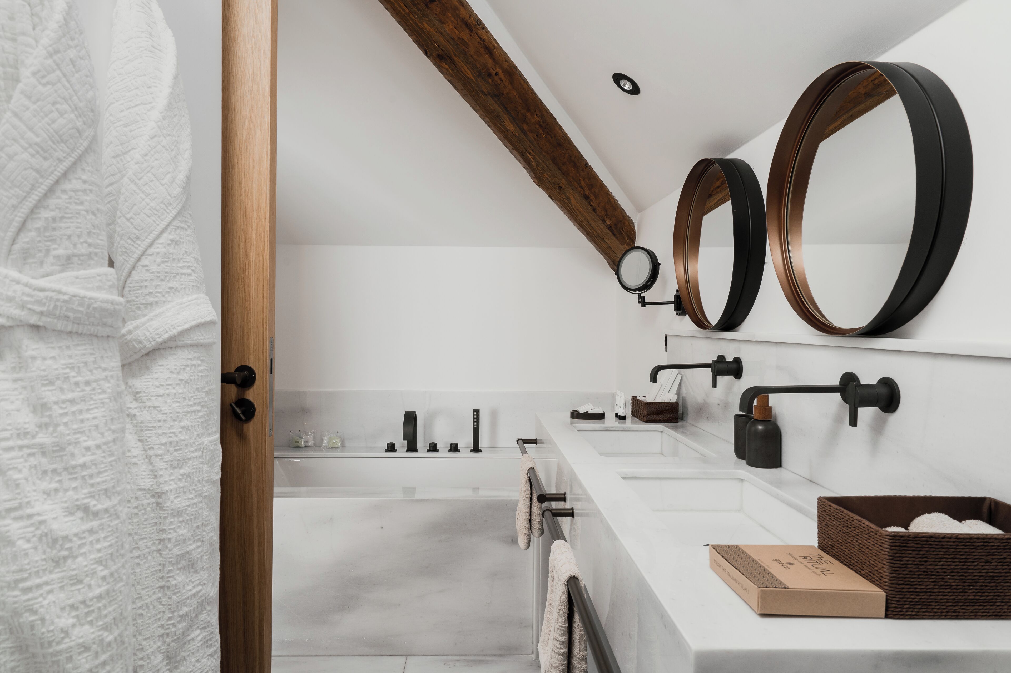 Un baño moderno con una viga de techo de madera, un espejo grande, un lavabo blanco y una bañera.
