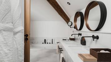 Un baño moderno con una viga de techo de madera, un espejo grande, un lavabo blanco y una bañera.