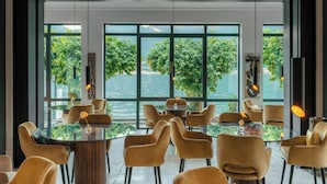 Un comedor moderno con mesas y sillas redondas, ventanas amplias con vista a zonas verdes y un cuerpo de agua.