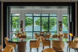 Un comedor moderno con mesas y sillas redondas, ventanas amplias con vista a zonas verdes y un cuerpo de agua.